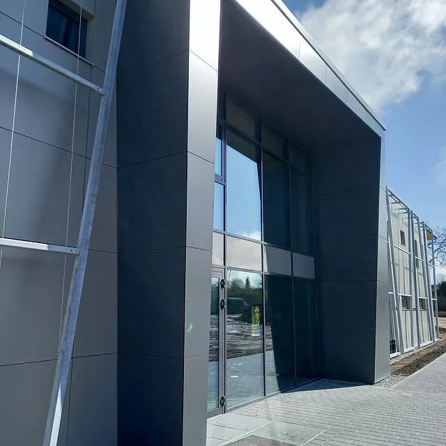 Eingangsbereich der Sporthalle in Engen mit moderner, dunkler Fassadenverkleidung und großen Glasflächen unter blauem Himmel