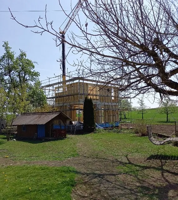 Neubau eines Einfamilienhauses in Holzbauweise mit vorgefertigten Ständerwänden und Decken, umgeben von grünem Garten und Bäumen