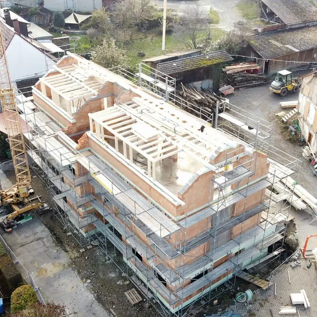 Neubau eines dreistöckigen Mehrfamilienhauses mit Holzrahmenkonstruktion und Gerüst, umgeben von älteren Gebäuden und Baugeräten