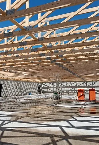 Innenansicht des Rohbaus eines Aldi-Neubaus mit sichtbaren Holzträgern und Schattenmustern auf dem Boden