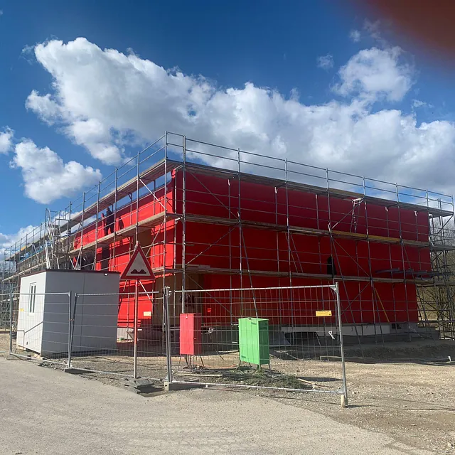 Rotes Feuerwehrgerätehaus im Bau mit Gerüst und Bauzaun in Konstanz-Dettingen unter blauem Himmel mit Wolken