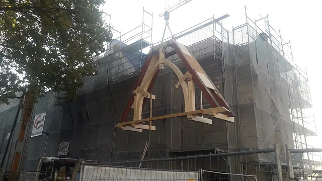 Holztragwerk wird mit Kran an ein eingerüstetes Gebäude bei einer Altbausanierung gehoben