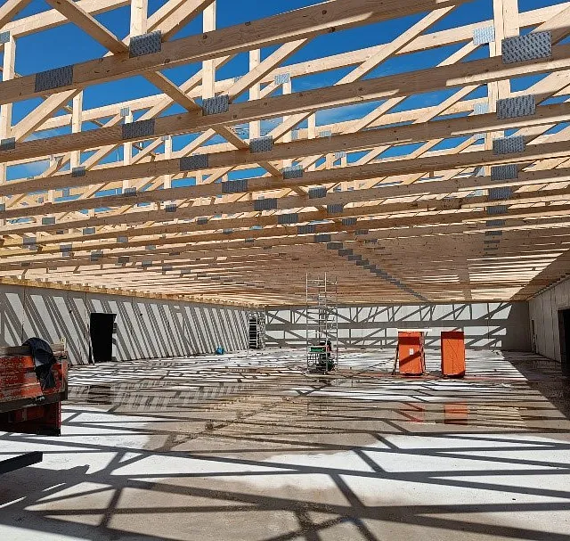 Innenansicht des Rohbaus eines Aldi-Neubaus in Mühlhausen-Ehingen mit sichtbaren Holz-Dachträgern und Betonboden, Baustellenausrüstung steht bereit