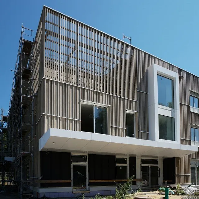 Neubau Kindergarten Jungerhalde Konstanz mit Außenwänden in Holz-Beton-Skelettbauweise, Fassade aus vertikalen Holzlatten, großes Vordach und Gerüst an der Seite