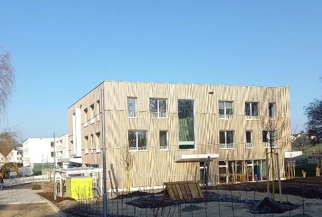 Neubau Kindergarten Jungerhalde Konstanz mit Außenwänden in Holz-Beton-Skelettbauweise, dreigeschossiges Gebäude mit vertikal verlaufender Holzfassade und mehreren Fenstern