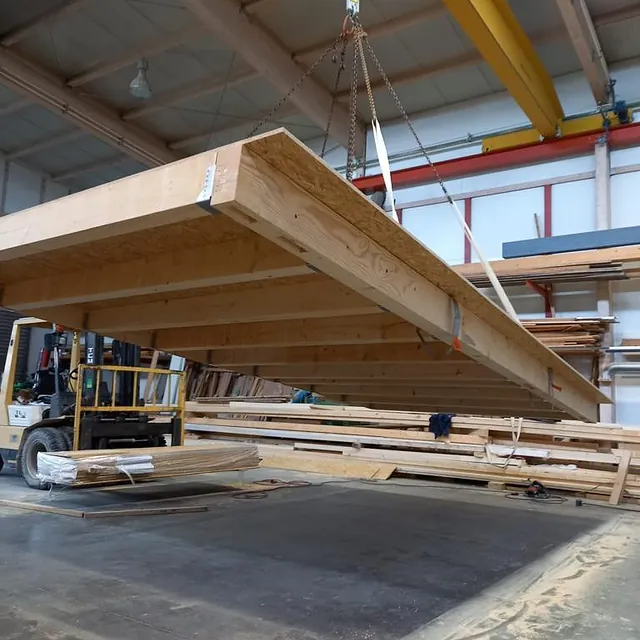 Großes vorgefertigtes Holz-Dachsegment wird in einer Werkhalle mit Kran für Dachsanierung gehoben