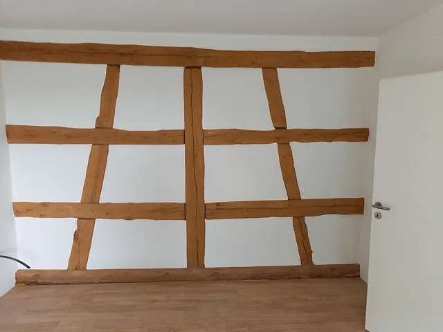 Innenwand mit sichtbarem Fachwerk aus Holzbalken in einem sanierten Altbau, weiß verputzt, mit Holzboden und geöffneter weißer Tür