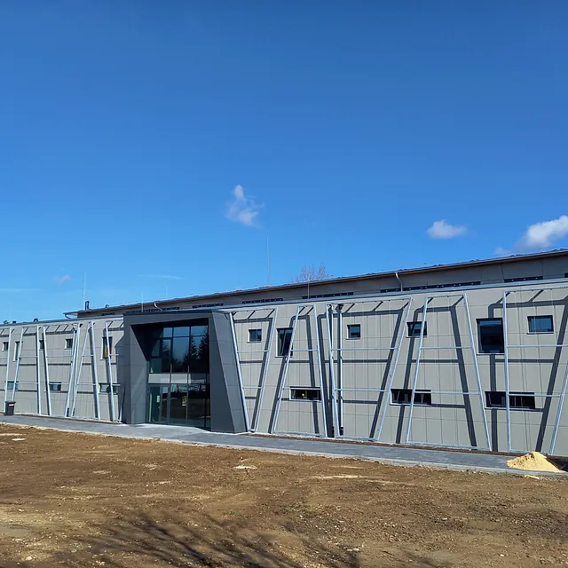 Sporthalle in Engen mit moderner Fassade aus grauen Paneelen und Metallrahmen, Baustelle mit unbefestigtem Boden im Vordergrund