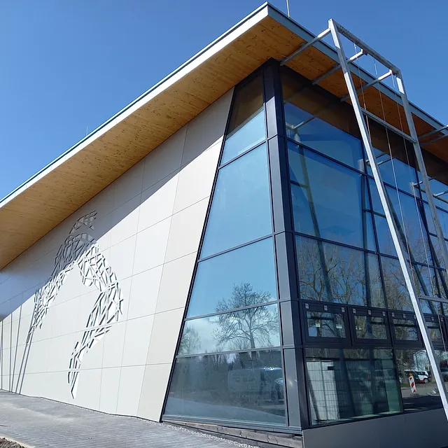 Sporthalle in Engen mit moderner Fassade aus Glas und hellen Paneelen, darunter eine abstrakte Sportler-Silhouette