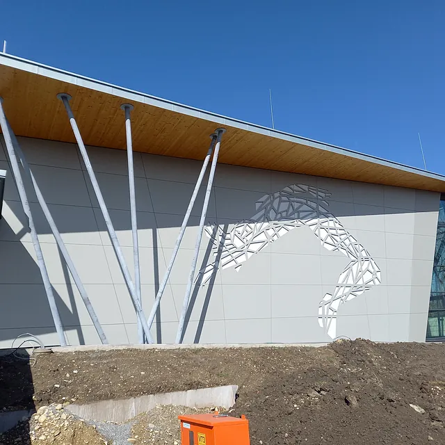 Fassade der Sporthalle in Engen mit moderner grauer Verkleidung und abstrakter Skulptur eines springenden Athleten aus Metallplatten