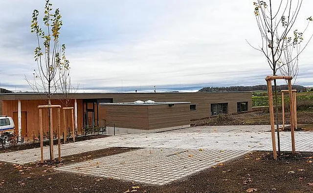 Neubau Kindergarten Steppachwiesle in Hilzingen, flaches Gebäude in Holzbauweise mit vorgefertigten Ständerwänden und Decken, umgeben von jungen Bäumen und gepflastertem Vorplatz