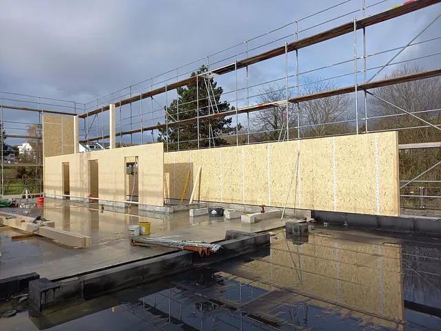 Baustelle eines Feuerwehrgerätehauses mit teilweise errichteten Holzplattenwänden und Gerüst im Hintergrund